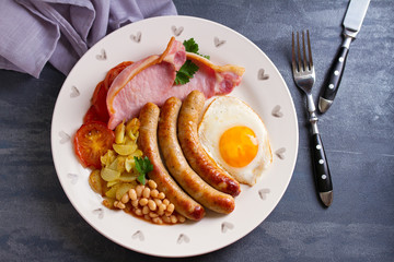 Full English or Irish breakfast with sausages, bacon, egg, tomatoes, fries and beans. Nutritious and healthy morning meal. View from above, top studio shot
