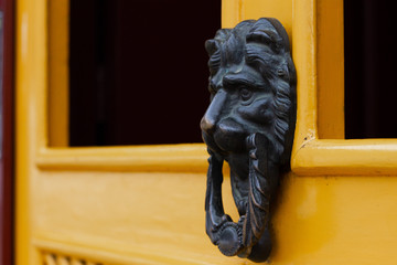 A metallic doorbell in the shape of a lion's head at a yellow door semi-opened in the historic city...