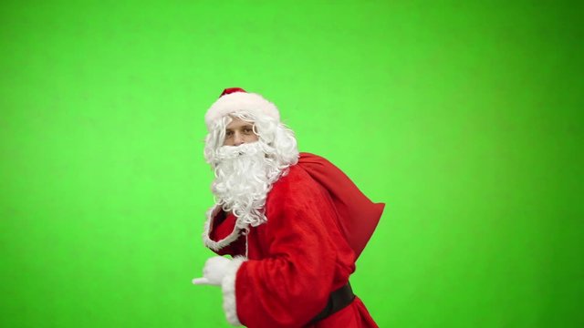 Santa Claus goes with gifts bag and looks into the distance on green background, Chroma key, 4k shot