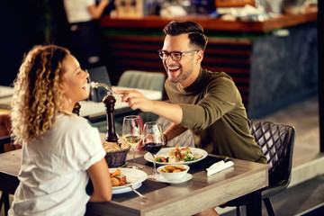 Cheerful man feeding his girlfriend while eating in a restaurant.
