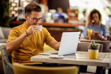 Young man drinking coffee while reading e-mail on a computer in a bar.