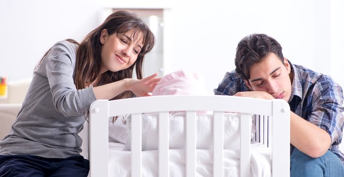 Young parents with their newborn baby near bed cot