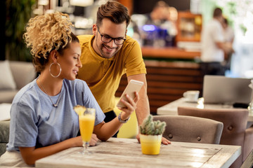 Young happy couple using smart phone in a bar.
