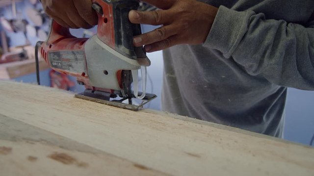 Crafts person uses a jigsaw to shape a surfboard