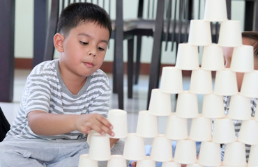 Kids Playing with white paper cups building a cup tower on floor.