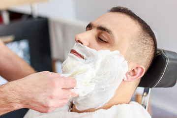 Hairdresser shaves a beard to a man with a razor in the barbershop