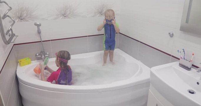 Little boy is putting on blue swimming glasses is jumping to the water in a bath.