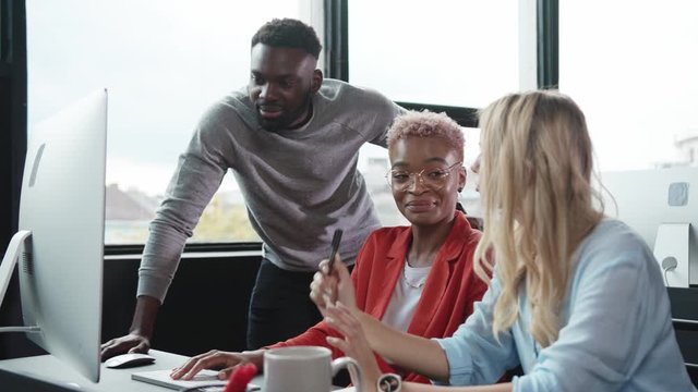 Team of young diverse business people cooperating at desktop computer in modern office. Three ambitious employees discussing financial plans for the company.
