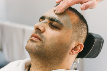 Male skin care in a beauty salon. Applying clay cleansing mask on a man's face