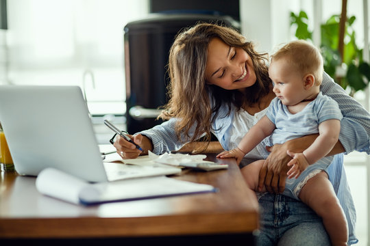 Happy Mother Talking To Her Baby While Working At Home.