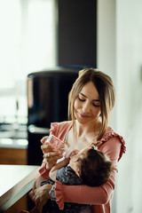 Young loving mother feeding her baby girl at home.