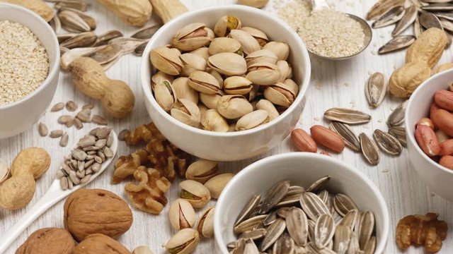 Assortment of nuts and seeds in white saucers on a white background.