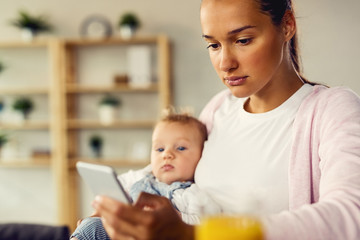 Young mother typing text message on mobile phone at home.