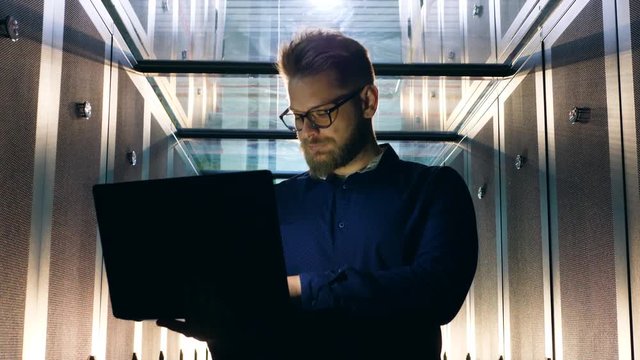 IT specialist types on laptop while working in server room.