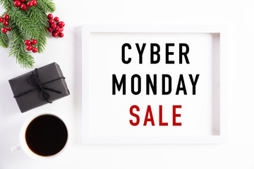 Top view of Cyber Monday Sale text on white picture frame with coffee cup, gift box and Christmas tree decoration, red berries on white background. Shopping concept and Cyber Monday composition.