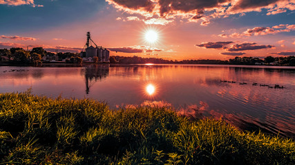 On the grassy shore of a rural southern Wisconsin lake with a view of the sun setting over the...