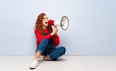 Redhead woman with overalls sitting on the floor shouting through a megaphone