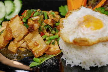 Close up and selected focus view of  Thai spicy Basil with crispy belly pork, Yardlong Bean and red chilli serve with streamed rice and fried egg.