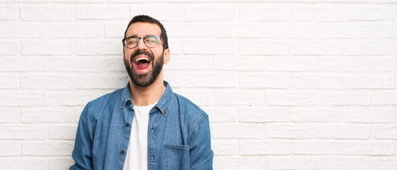 Handsome man with beard over white brick wall shouting to the front with mouth wide open