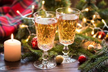 Two glasses of champagne on a wooden table with a candle and Christmas balls and fir branches