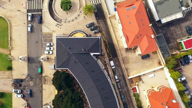 Aerial, top down, drone shot, over buildings, the N6 road, railway tracks and the Tamariz Beach, towards waves on the Atlantic ocean, on a cloudy day, in Estoril, Lisbon, Portugal