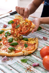 Hand of a woman taking a slice of a pizza viewed from above on rustic turquoise boards