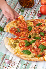 Hand of a woman taking a slice of a pizza viewed from above on rustic turquoise boards