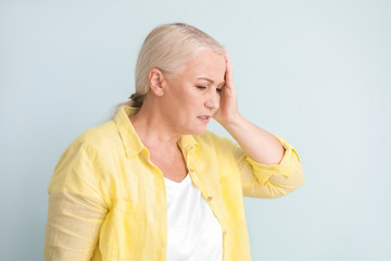 Mature woman suffering from headache on light background