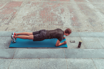male athlete stands bar, training abs muscles on summer day city. Mat yoga gymnastics. Shaker with water protein. Mobile phone timer app. Active lifestyle fitness motivation free space text.