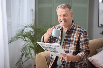 Portrait of stylish mature man with newspaper and cup of coffee resting at home