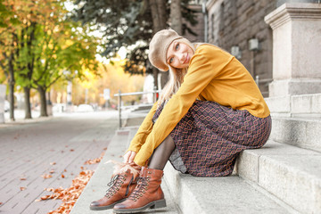 Beautiful young woman sitting on steps in autumn city
