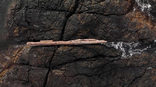 Overhead aerial shot of driftwood on a rugged rock outcropping with waves crashing around it. - 4K 24FPS