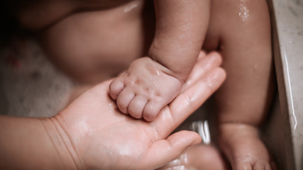 Baby hand on mother's hand. Pretty baby boy taking a bath.