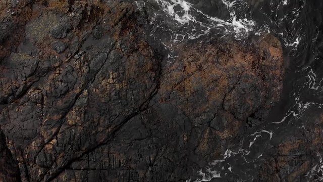 Overhead aerial shot of driftwood on a rugged rock outcropping with waves crashing around it. - 4K 24FPS
