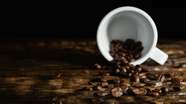 beverage background of roasted coffee beans with laying coffee cup on wooden table