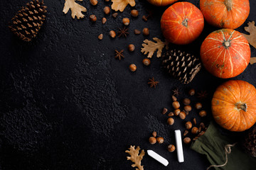 Autumn frame of pumpkins, tree leaves, hazelnuts on a black textural background. Crayons for...