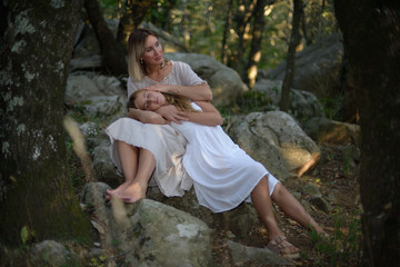 Woman in a forest sitting and relaxing with her daughter lying on her legs as the sun goes down