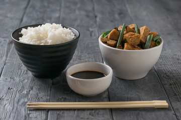 A bowl of rice, a bowl of tofu and a bowl of soy sauce.