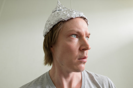 Face of young man with tin foil hat thinking inside the room