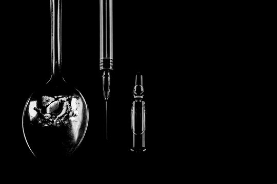 Drugs. Syringe, spoon with heroin and ampoule on a black background.