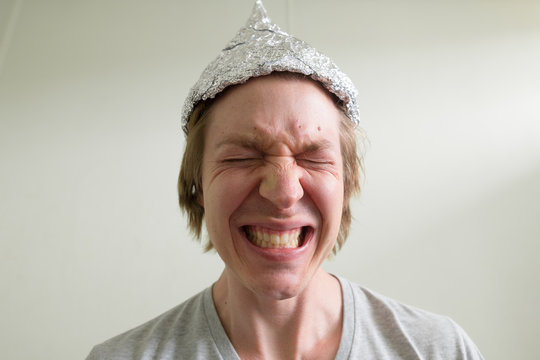 Face of stressed young man with tin foil hat getting scared inside the room