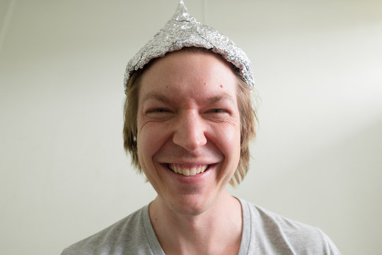 Face of happy young man with tin foil hat smiling inside the room