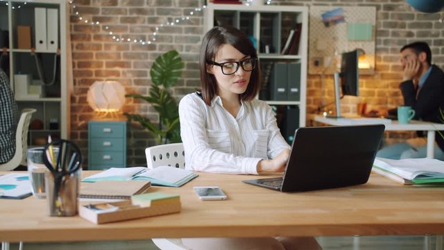 Happy businesswoman is working in office late at night using computer writing in notebook smiling enjoying work. People, workaholism and business concept.