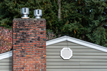 Exterior wall of suburban house, old brick chimney with chimney vents, attic fan exhaust vent on...