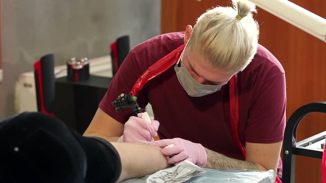 Cool tattoo master with professional tattoo machine makes a tattoo for a girl in a stylish tattoo parlor. Slow motion.