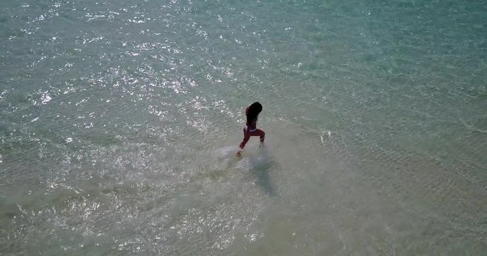 Beautiful young girl in white bikini running in crystal shallow water off the coast of tiny luscious island in Maldives