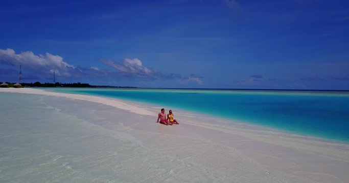 Couple relaxing off the shore of tiny tropical island on yellow inflatable, with girl wearing sunglasses and black bikini