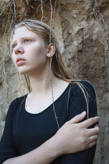 portrait of young girl in black dress with wet long blonde hair posing outdoors
