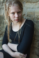 portrait of young girl in black dress with wet long blonde hair posing outdoors