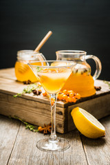 Hot autumn cocktail with sea buckthorn and orange juice in martini glass on the rustic background....